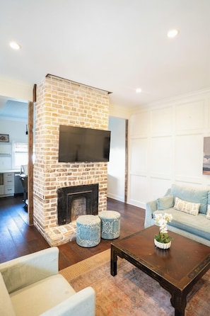 A living room with a brick fireplace, a sofa, a coffee table, and a TV mounted above the fireplace.
