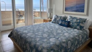 A bedroom with a large bed, a view of the ocean through glass doors, and a framed picture on the wall. - See The Sea 2-Ocean Front, Dining on Patio, 2 bd! (San Diego)