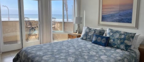 A bedroom with a large bed, a view of the ocean through glass doors, and a framed picture on the wall.