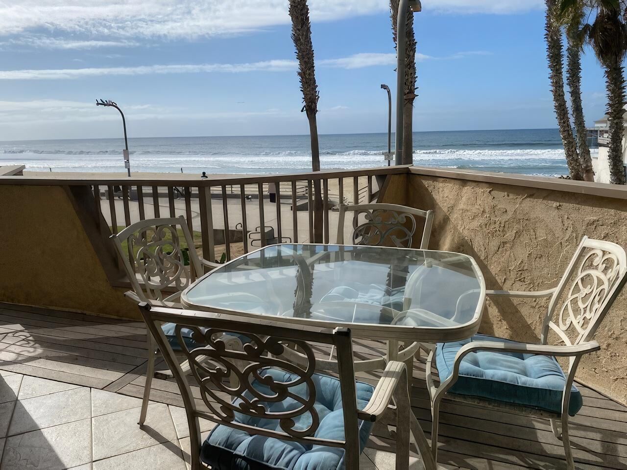 A glass-top table with metal chairs and blue cushions on a patio overlooking the ocean.