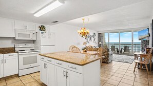 A kitchen with white cabinets, a microwave, and a stove. There is a dining area with chairs and a table.