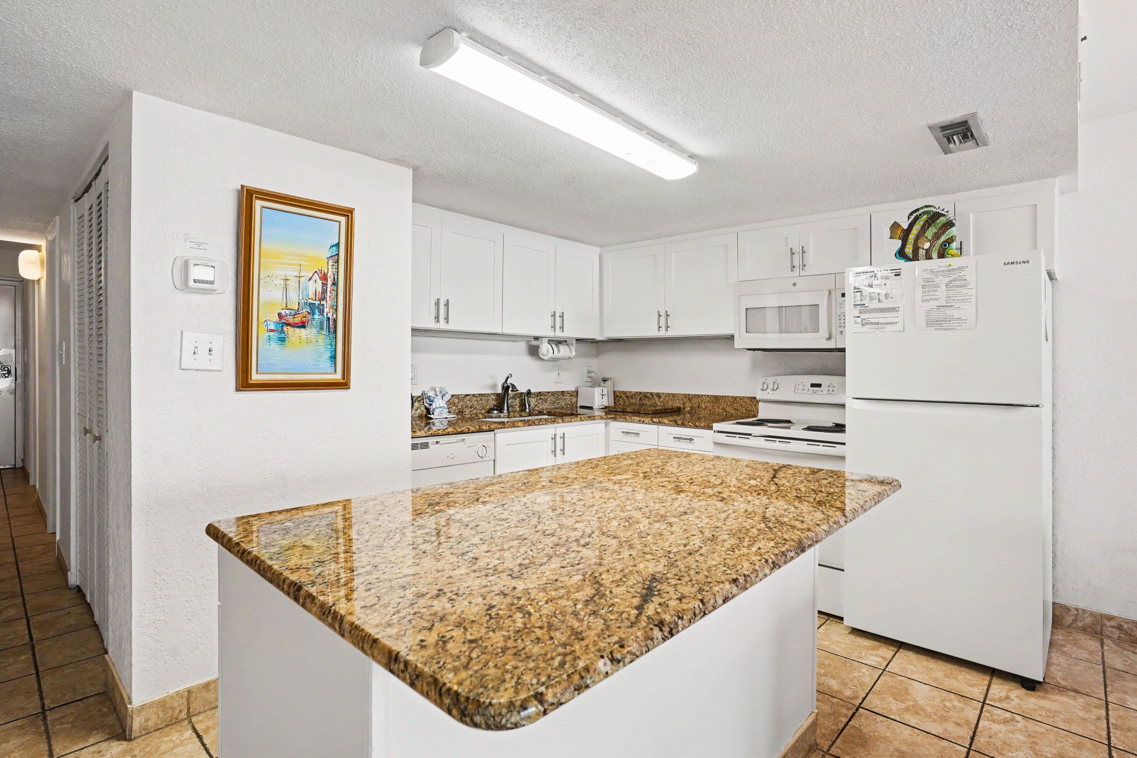 A kitchen with white cabinets, a granite countertop, a microwave, and a refrigerator.