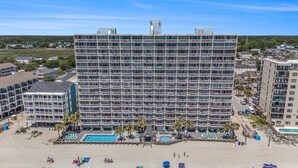 A multi-story hotel with balconies, a pool area, and beach access.
