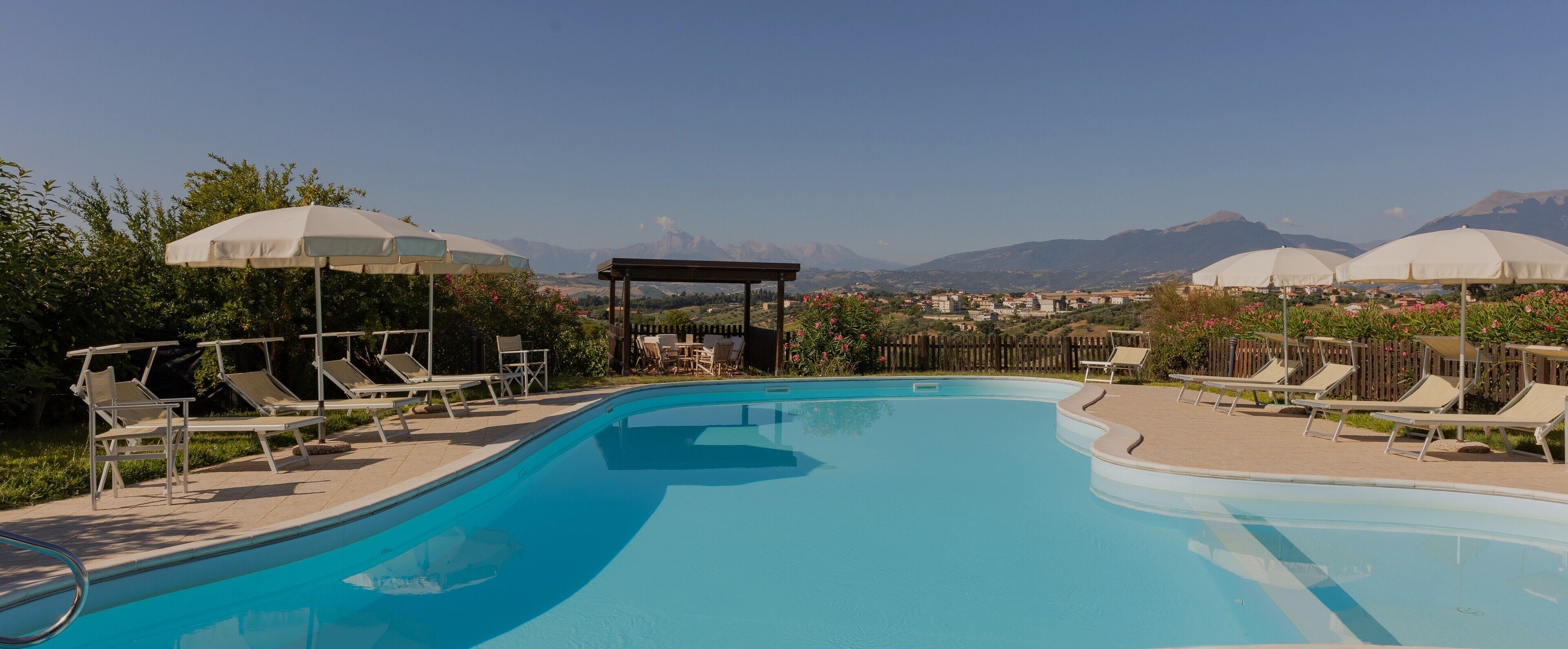 Une piscine entourée de chaises longues et de parasols, avec une végétation luxuriante et des montagnes en toile de fond.