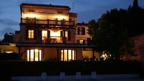 Une maison à deux étages avec une piscine et des chaises longues devant.