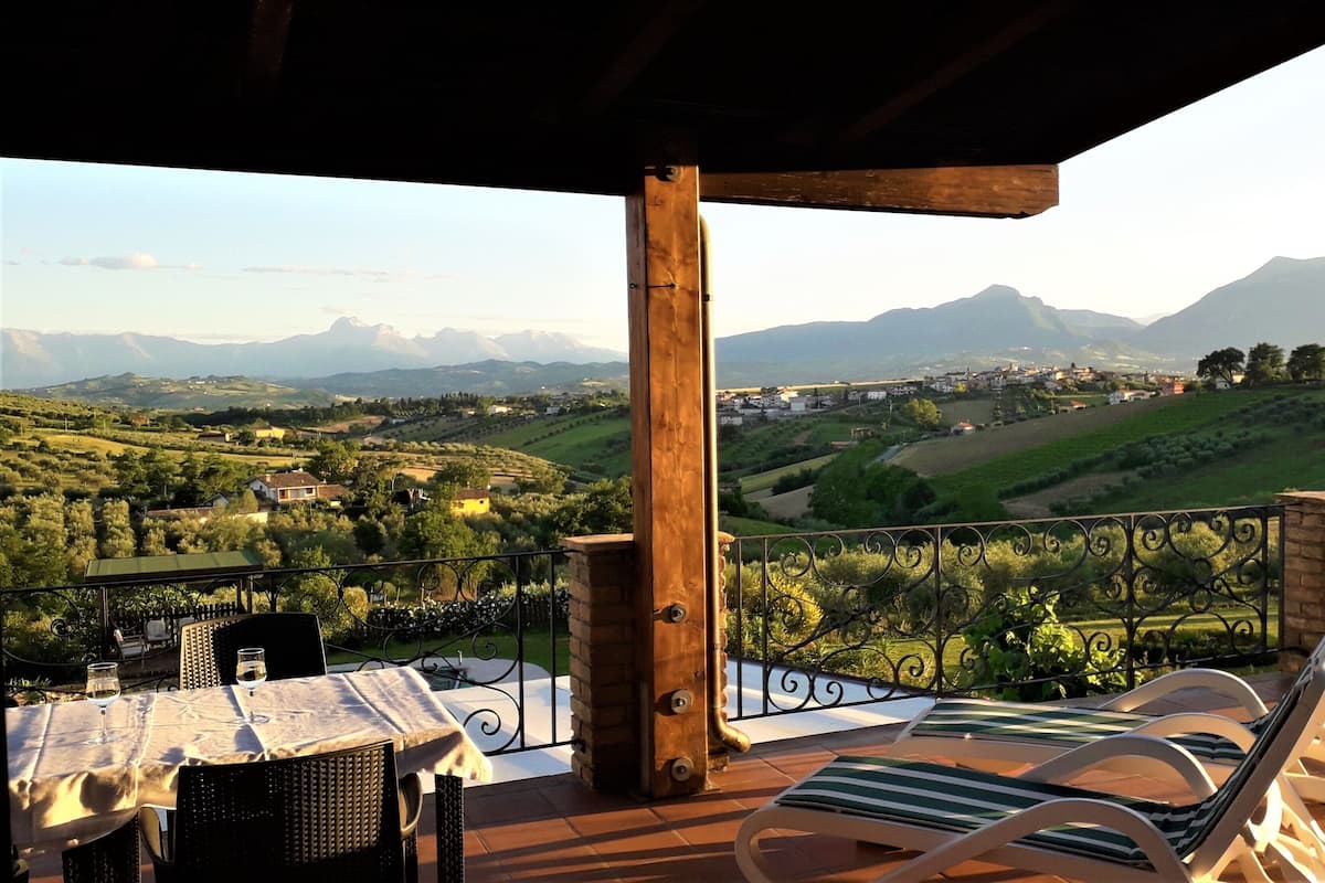 Une terrasse avec une table dressée pour deux personnes, offrant une vue panoramique sur un paysage magnifique, avec des montagnes et un village.