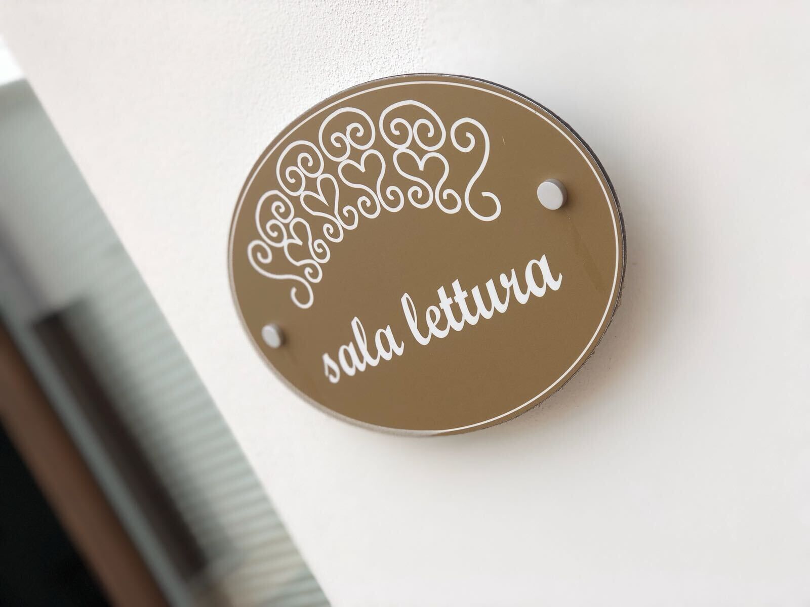 A circular sign with decorative swirls and the text 'sala lettura' mounted on a wall.