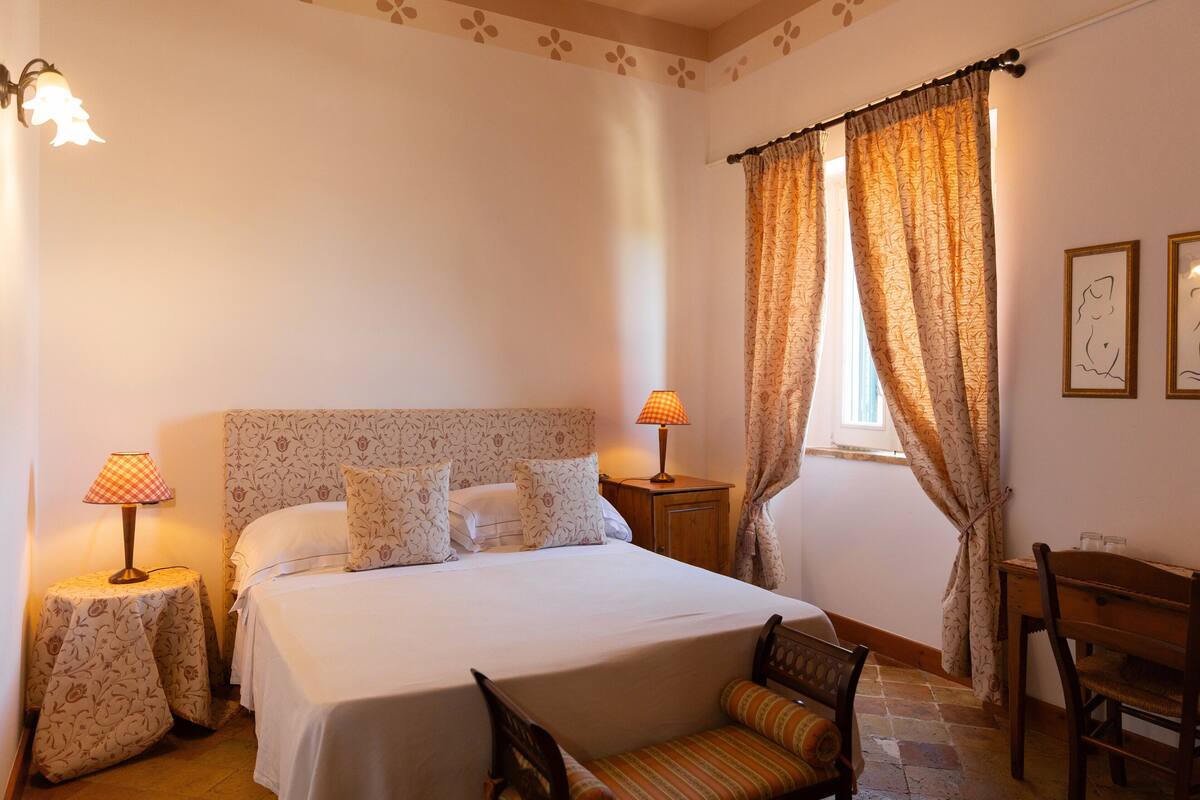 Une chambre à coucher bien rangée, avec un lit, deux tables de chevet dotées de lampes, une chaise et une petite table.
