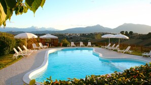 Une piscine entourée de chaises longues et de parasols, avec une végétation luxuriante et des montagnes en toile de fond.