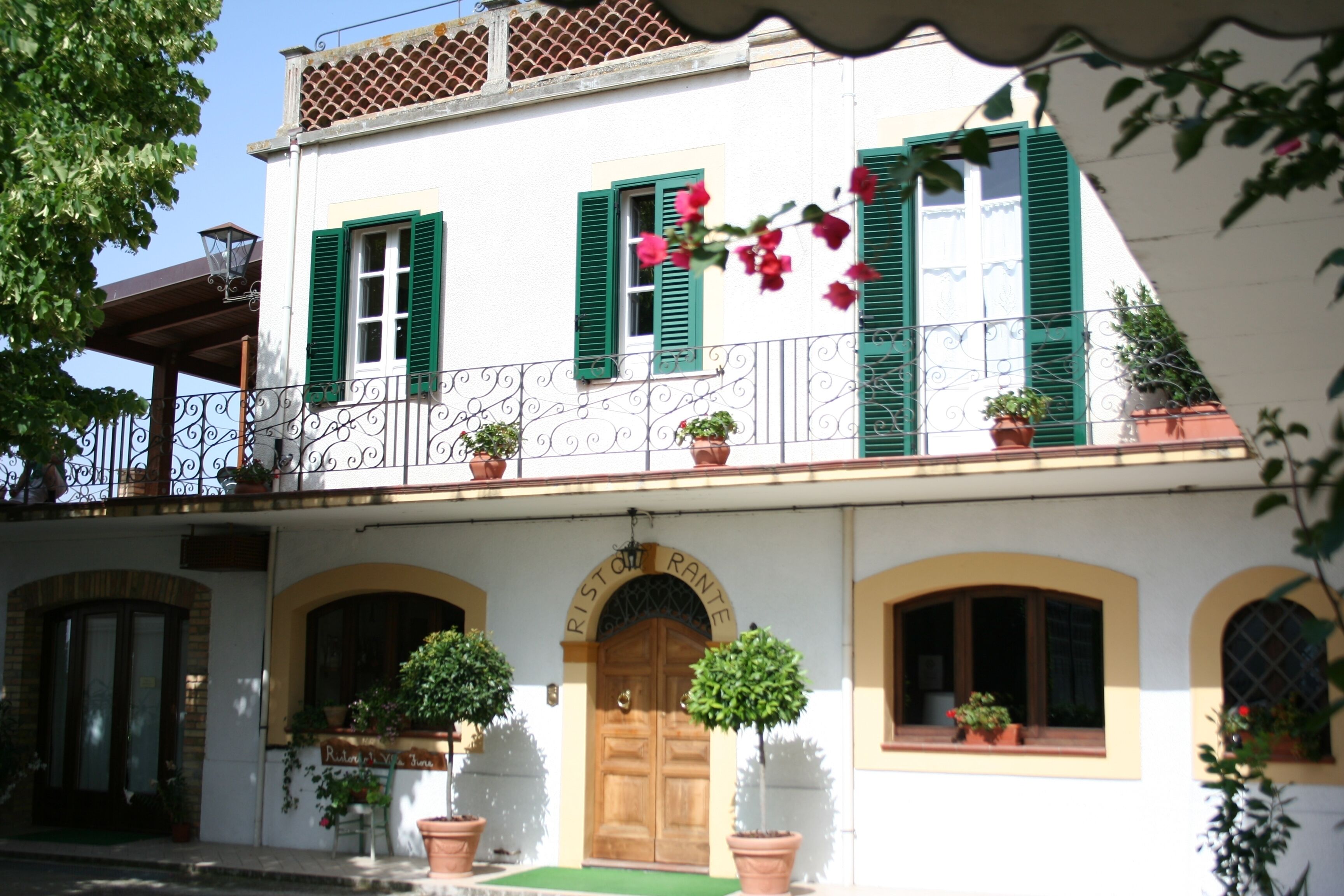 A two-story building with a balcony, green shutters, and potted plants.