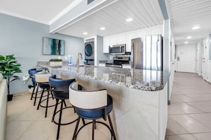 Una cocina moderna con encimera de granito, electrodomésticos de acero inoxidable y taburetes de bar.