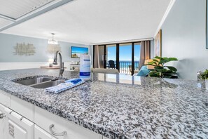 Una cocina moderna con encimeras de granito, un lavamanos de acero inoxidable y un amplio ventanal con vistas a la playa.