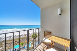 Un balcón con una mesa y una silla de madera, con vista a una playa y una piscina.