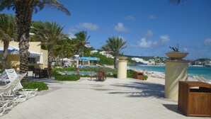 A resort pool area with lounge chairs, palm trees, and a view of the beach. - Spacious 1800 Sq Ft Ocean View Condo (Oyster Pond)
