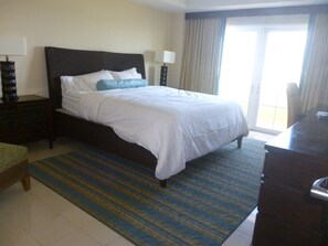 A hotel room with a large bed, a wooden nightstand, a desk, and a view of the outdoors through a sliding door.