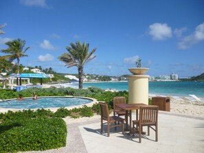 A pool area with lounge chairs and a table, overlooking a beach and ocean.