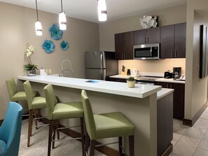 A modern kitchen with a central island, bar stools, stainless steel appliances, and decorative wall art. - Spacious 1800 Sq Ft Ocean View Condo (Oyster Pond)
