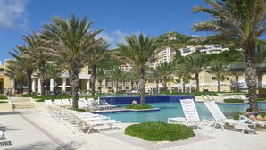 A resort pool area with sun loungers, palm trees, and a clear blue sky. - Spacious 1800 Sq Ft Ocean View Condo (Oyster Pond)