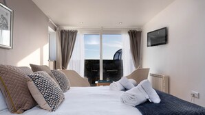 A modern hotel room with a large bed, a flat-screen TV, and a view of the outdoors through the window. - 3 Bedroom Beachside Property with Glass Pod! (Praa Sands)