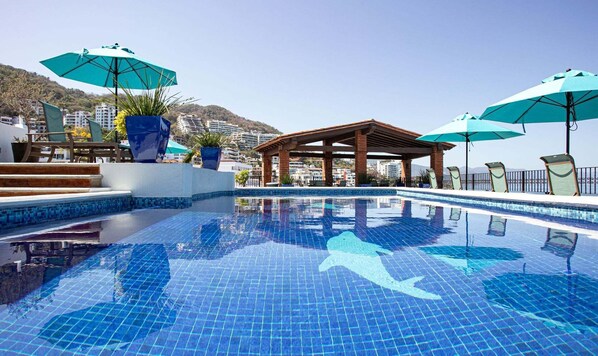 Une piscine d’un bleu éclatant, avec des marches carrelées menant à l’intérieur, entourée de chaises longues et de parasols.