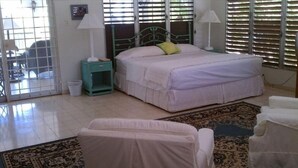 Une chambre à coucher avec un lit, deux tables de chevet, une petite table d’appoint verte, une chaise blanche et un tapis à motifs.