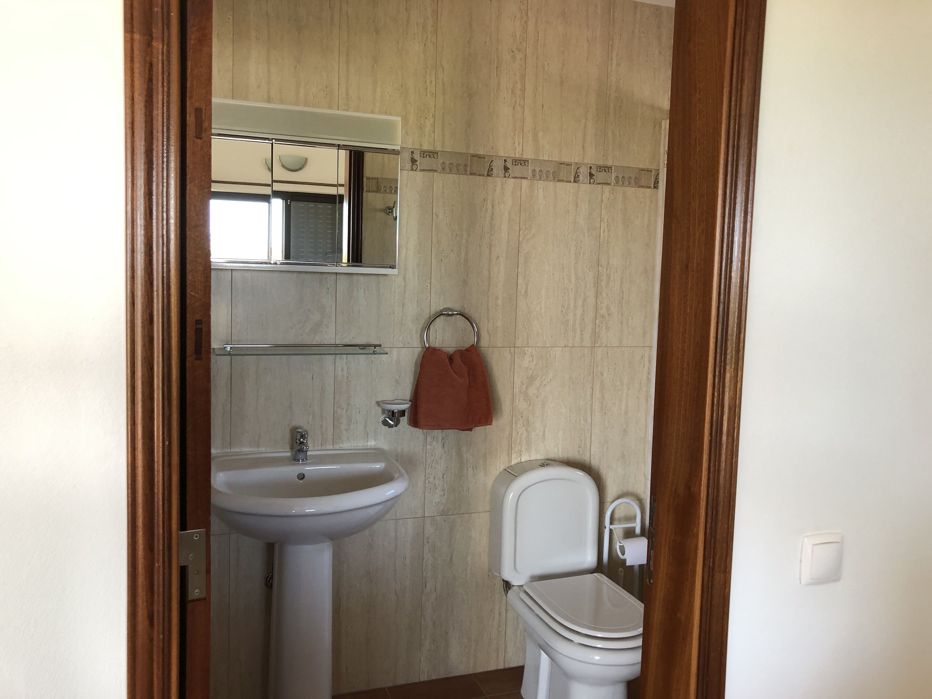 Een badkamer met een wastafel op een voetstuk, een toilet en een spiegel boven de wastafel.