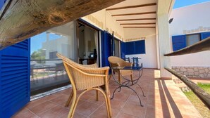An outdoor patio with wicker chairs and a table, a glass door leading inside, and a view of a building with blue shutters. - Traditional Portuguese house with lot of privacy and space. (Carvoeiro lagoa)