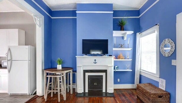 Une pièce aux murs bleus, avec une cheminée blanche, un téléviseur et une table en bois entourée de chaises.