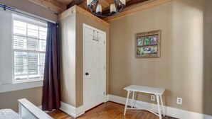 Une pièce avec un plafond en bois, une porte blanche, une petite table blanche et une fenêtre avec des rideaux.