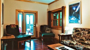 A cozy living room with a wooden floor, a green armchair, a sofa with a patterned cover, a coffee table, and a poster on the wall. - Beautiful Views of The Great Smoky Mountains From Anywhere Indoors or Out! (Bryson City)