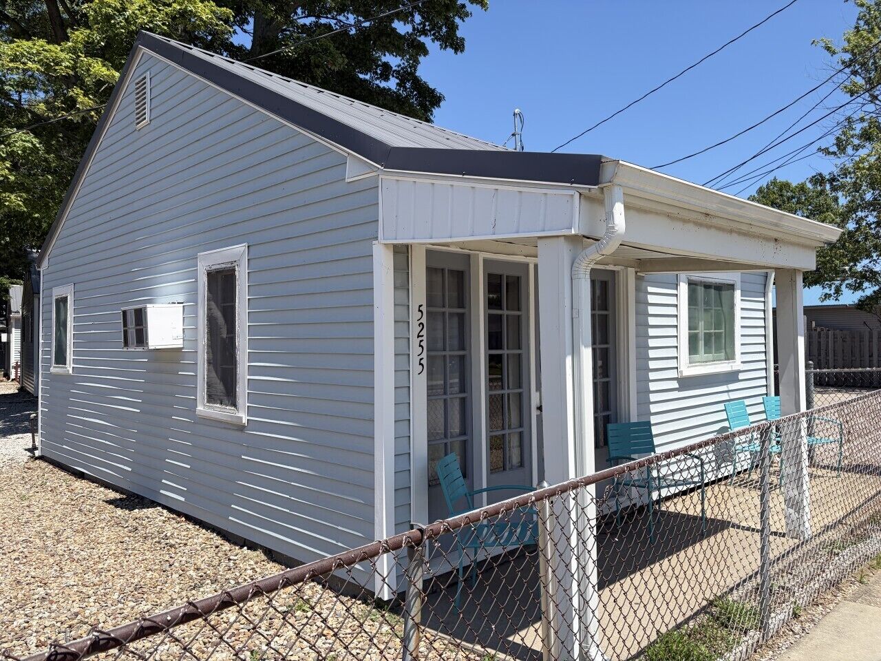 A small, single-story house with a porch, a number '5235' on the door, and a chain-link fence in front.