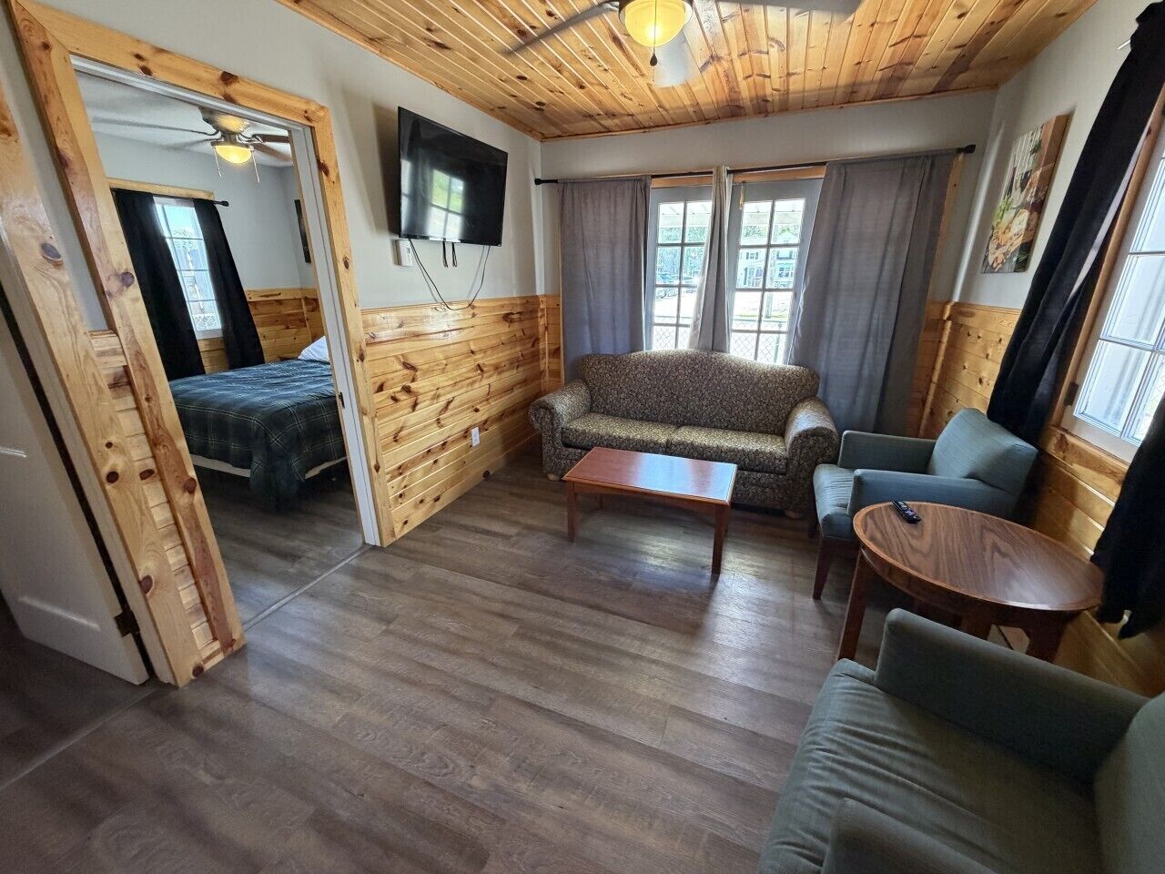 A room with wooden walls, a sofa, a coffee table, a TV, and a bed.