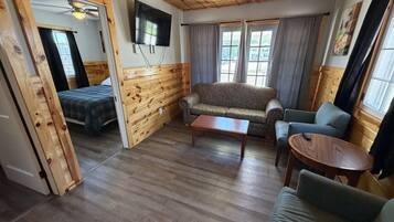 A room with wooden walls, a sofa, a coffee table, a TV, and a bed.