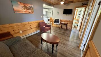 A cozy room with a wooden ceiling, a sofa, a table, and a kitchen area visible through an open door.