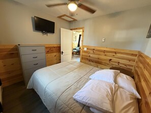 Una camera da letto con un letto, una cassettiera, una televisione e una ventola a soffitto.