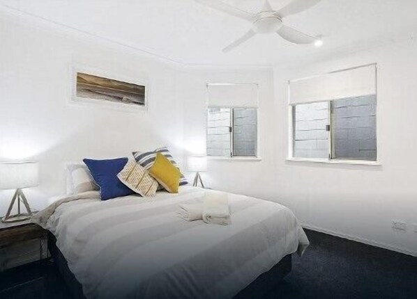 Une chambre à coucher avec un lit, des tables de chevet, un ventilateur de plafond et des fenêtres.
