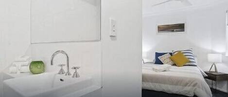 A modern bathroom with a large mirror, a sink, and a green soap dispenser. The room has a white color scheme and a ceiling fan.