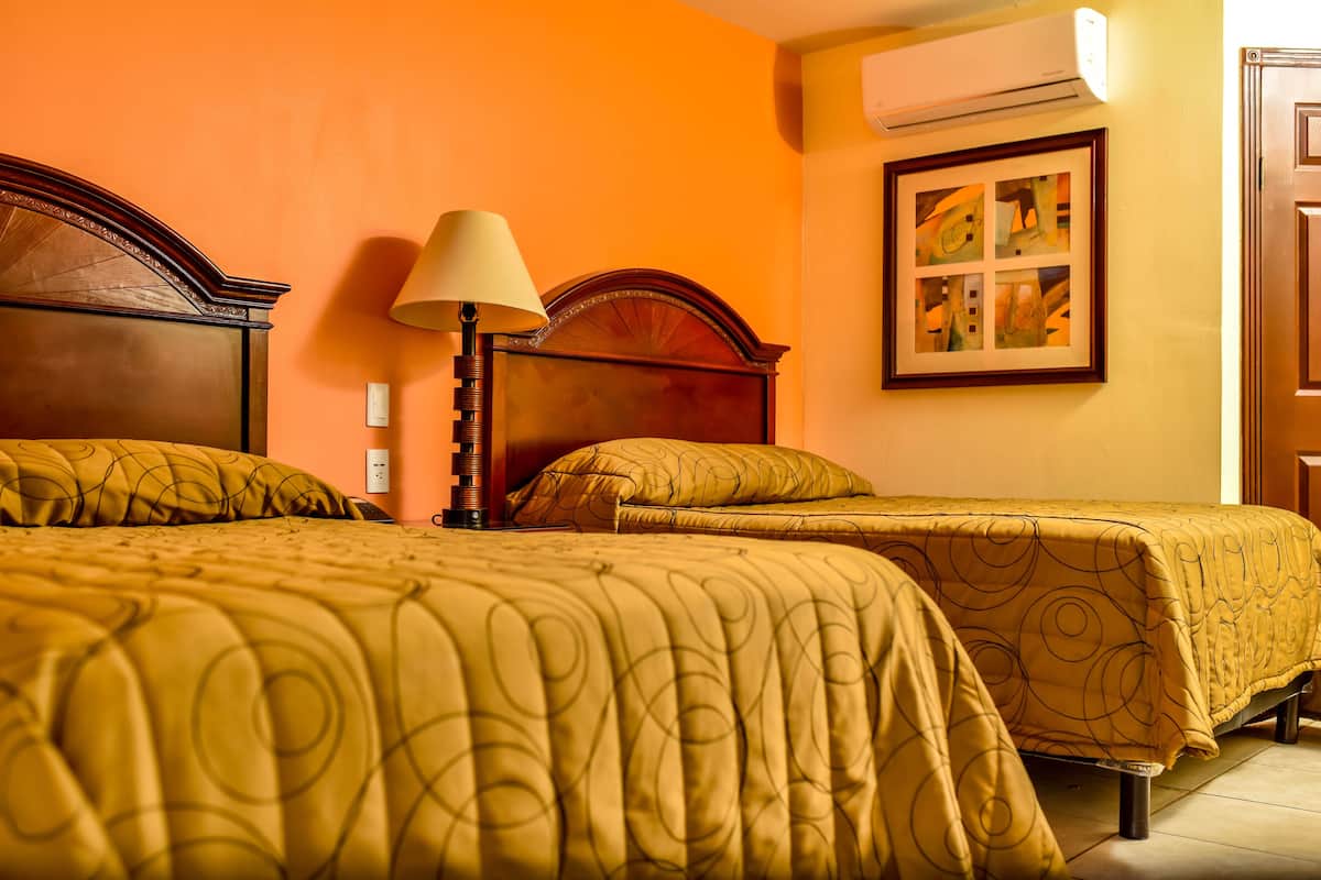 A hotel room with two beds, a lamp, and a framed artwork on the wall.