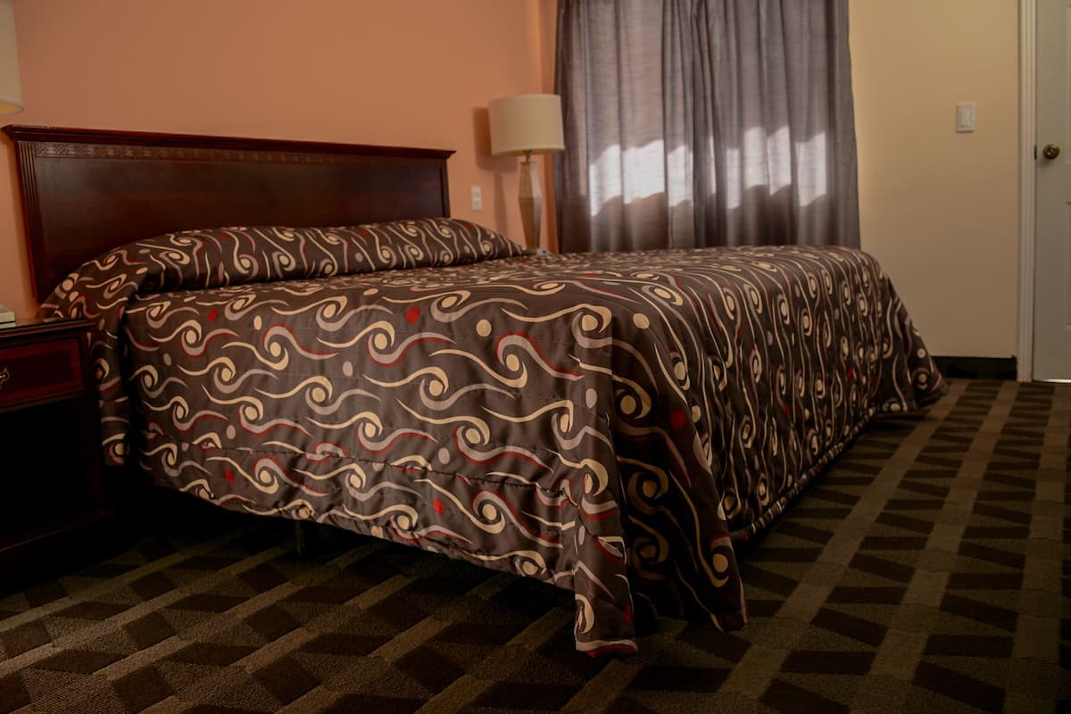 A hotel room with a large bed, a wooden headboard, a nightstand, a lamp, and a door.