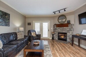 A living room with a fireplace, a sofa, a coffee table, and a TV mounted on the wall.