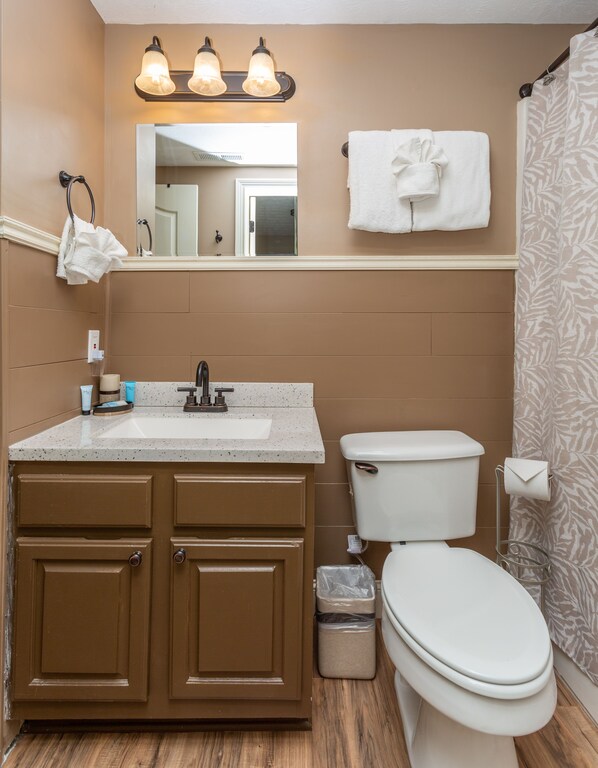A bathroom with a sink, mirror, towel rack, toilet, and shower curtain.