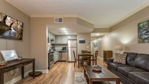 Eine moderne Küche mit Edelstahlgeräten, ein Essbereich mit Holztisch und -stühlen sowie ein Wohnzimmer mit Ledersofa und Wand-TV.