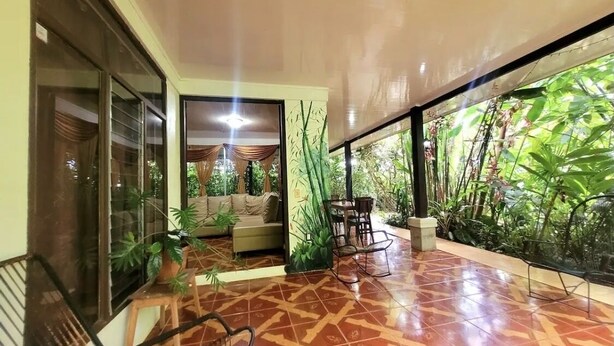 A spacious indoor area with a patterned floor, a sofa, a table, and chairs. There are large windows on one side and a door on the other.