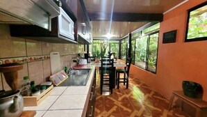 A kitchen with a tiled backsplash, a sink, a stove, and a dining area with chairs and a table.