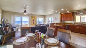 A dining area with a table set for four, a kitchen with wooden cabinets, and a view of the ocean through large windows.