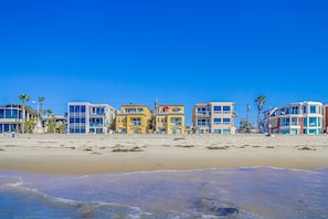 Un hotel frente a la playa con varias edificaciones, una playa arenosa y cielos azules despejados.