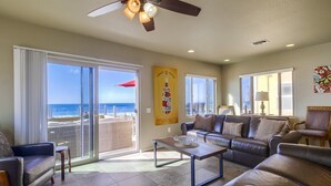 A spacious living room with a large sliding glass door leading to a balcony with a view of the ocean. There is a ceiling fan, a coffee table, and a sofa.