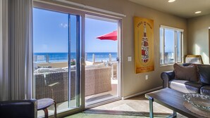 A room with a glass door leading to a balcony with a wicker chair and a red umbrella. There is a poster on the wall and a leather sofa.