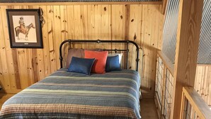 A bedroom with a metal bed frame, wooden walls, and a framed picture on the wall.