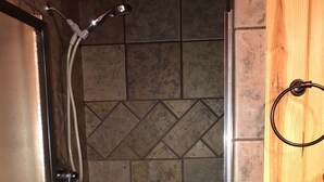 A shower area with a tiled wall, a wooden door, and a metal shower head.